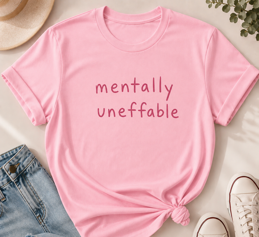 Pink t-shirt with 'mentally unefable' text on a light surface with jeans and shoes.
