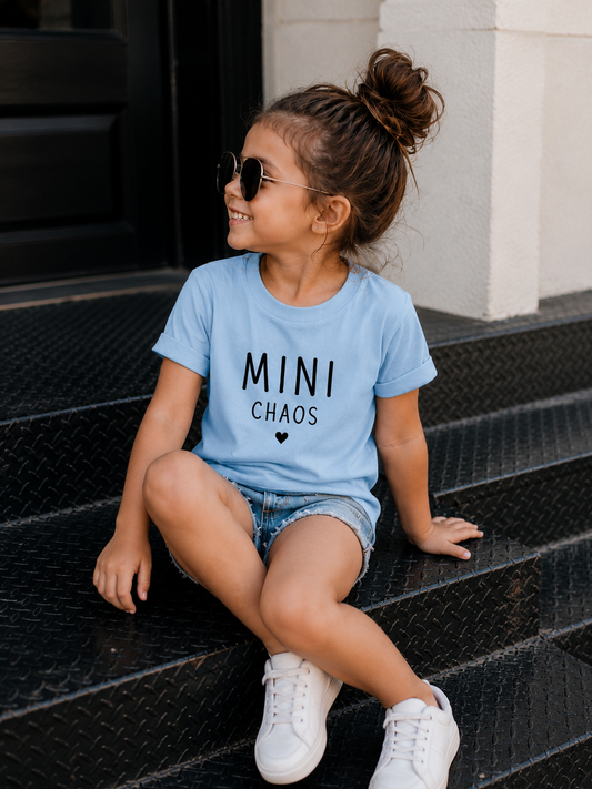 Young girl wearing the Mini Chaos blue cotton graphic t-shirt with white typography, paired with denim shorts and white sneakers.