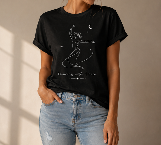 Person wearing a black t-shirt with a graphic design and text, 'Dancing with Chaos' standing against a beige wall.