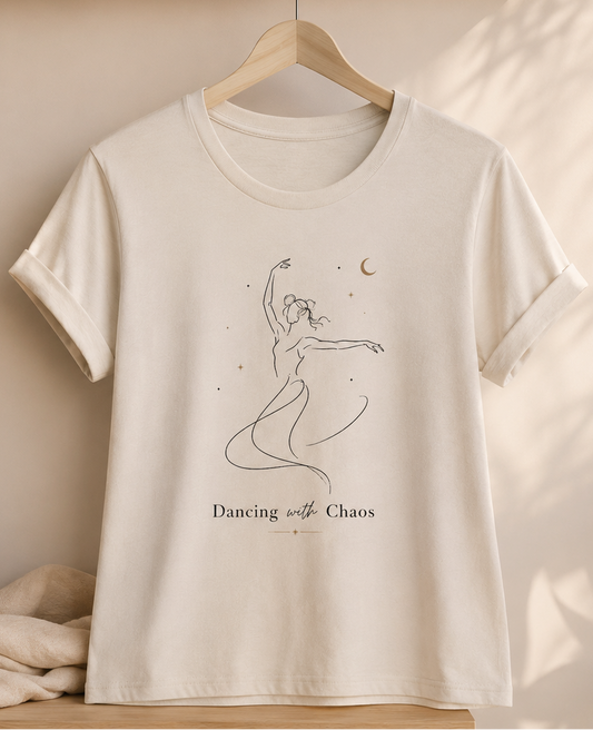 Beige t-shirt with a graphic of a dancer and text 'Dancing with Chaos' on a wooden surface.