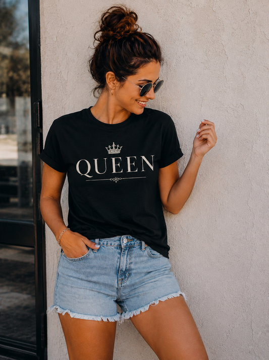 Woman wearing a black 'QUEEN' t-shirt and denim shorts against a light-colored wall.