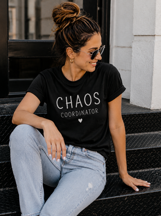 Woman wearing a black t-shirt with 'CHAOS COORDINATOR' text, sitting on steps.
